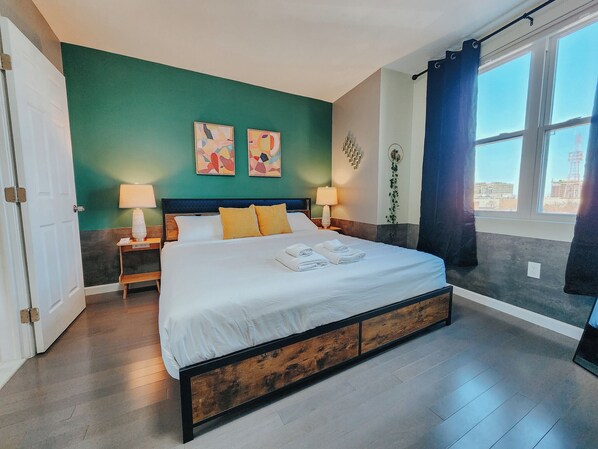 A modern hotel room with a large bed, two bedside tables with lamps, a green accent wall, and a window with curtains.
