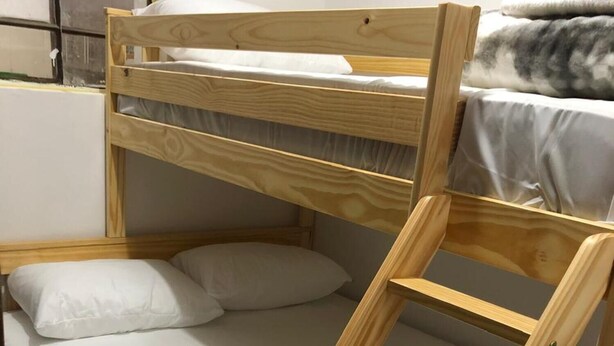 Una cama litera con estructura de madera, ropa de cama blanca y un gato durmiendo en la cama inferior.
