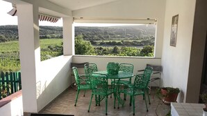 A patio with a table and chairs, a view of greenery, and a tiled floor.