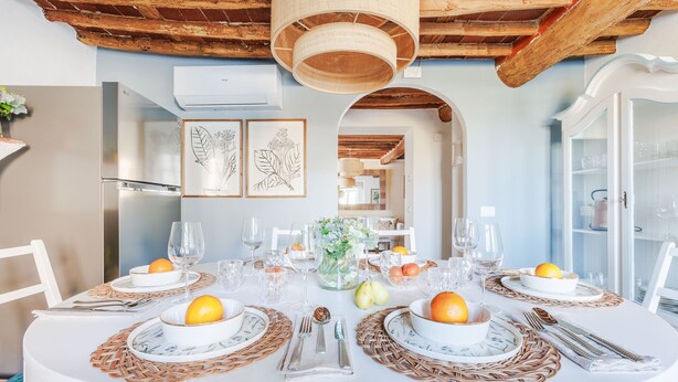 A dining table set for four with white tablecloths, woven placemats, and a central floral arrangement. - Villa Podere Falcione (Lucca)