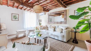 A living room with a white sofa, a round coffee table, and a large potted plant. - Villa Podere Falcione (Lucca)