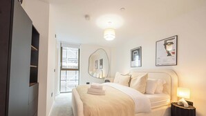 Een slaapkamer met een groot bed, een nachtkastje met een lamp, een kledingkast en een grote spiegel aan de muur.