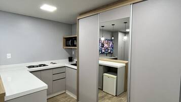 Cocina compacta con microondas, estufa y alacenas, un refrigerador pequeño y un armario con espejo.