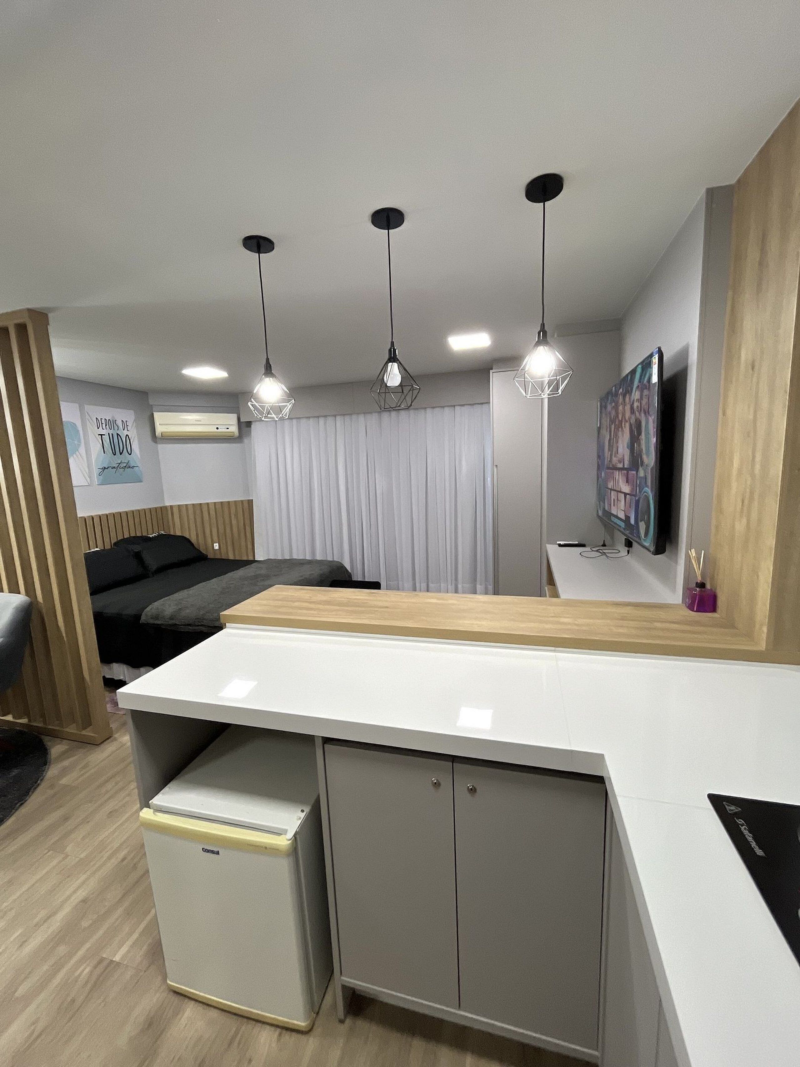 A modern room with a kitchenette, a bed, a desk, and a TV.