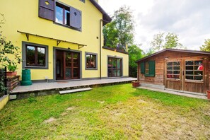 Un bâtiment jaune à deux étages, avec une structure en bois sur le côté droit, une cour verdoyante et un ciel dégagé.