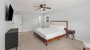 Une chambre à coucher avec un lit, un ventilateur de plafond, une commode, un téléviseur et une fenêtre.