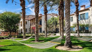 A courtyard with palm trees, a hammock, and a building with blue shutters. - Stylish Desert King Room w/ Balcony + Pool View (La Quinta)