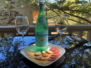 Une table en verre avec une bouteille d’eau pétillante Pellegrino, deux verres et une assiette contenant du fromage et du salami.