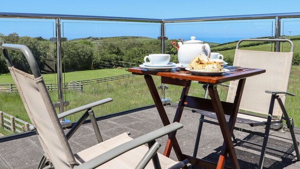 Une terrasse avec une table préparée pour le thé, des chaises et une vue magnifique sur la mer.