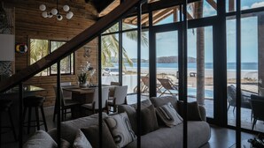 Ein geräumiger Wohnbereich mit großem Fenster mit Blick auf Strand und Pool.