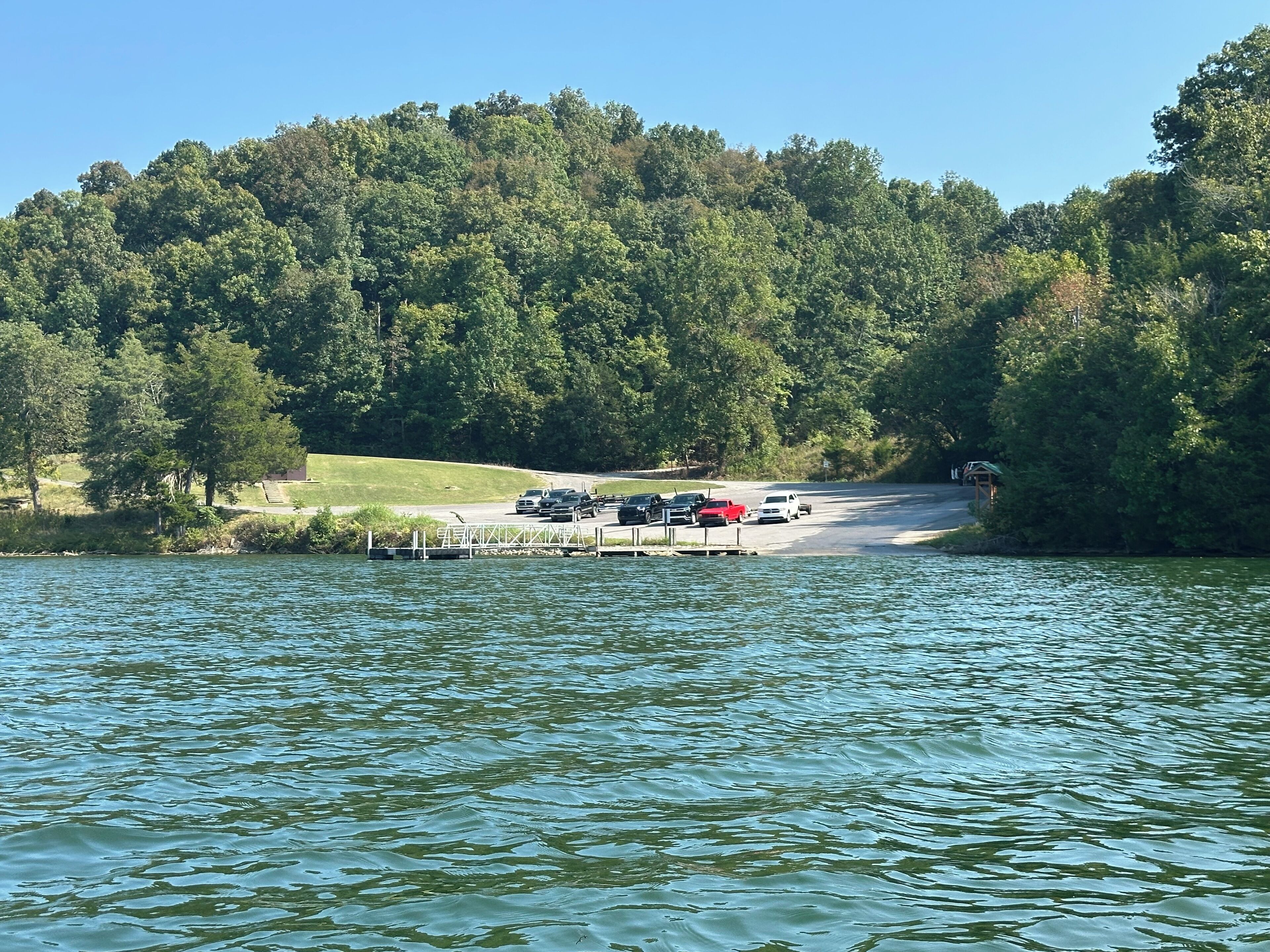 A lakeside parking area with vehicles and a dock extending into the water.