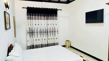 A bedroom with a bed, a ceiling fan, a window with curtains, a bedside table, and a wall-mounted TV.