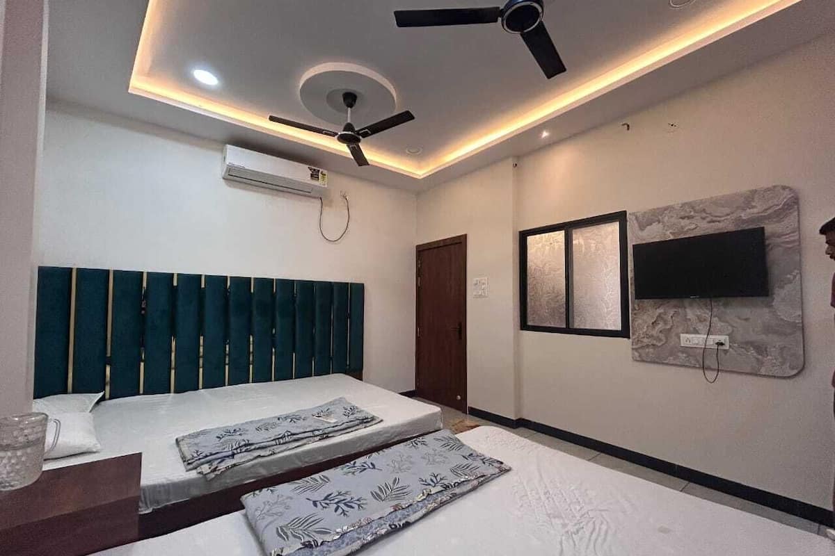 A modern bedroom with a bed, a ceiling fan, an air conditioning unit, a TV mounted on the wall, and a door.