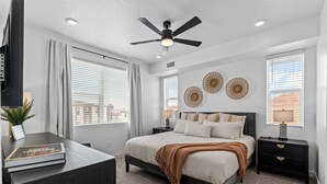 Ein Schlafzimmer mit einem Bett, Nachttischen, einem Deckenventilator und Wanddekoration.