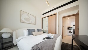 Une chambre d’hôtel moderne avec un lit bien fait, une table de chevet avec une lampe, un grand miroir et une vue sur la cuisine.