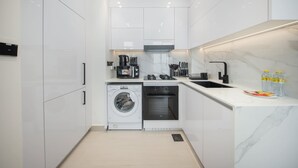 Une cuisine moderne avec des meubles blancs, un lave-linge et un sèche-linge intégrés, une cuisinière et un évier.