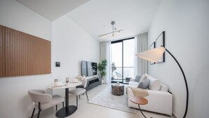 Un salon moderne avec un canapé blanc, une table à manger avec des chaises, un téléviseur et une grande fenêtre avec des rideaux.