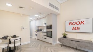 A modern kitchen with a dining area, a large "BOOK ME" sign on the wall, and a grey console table with a plant. - Vibrant Studio in JLT Sleeps 4 With Lake Views (Dubai)