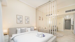 A modern hotel room with a large bed, a bedside table, a nightstand, a mirror, and a view of the bathroom. - Vibrant Studio in JLT Sleeps 4 With Lake Views (Dubai)