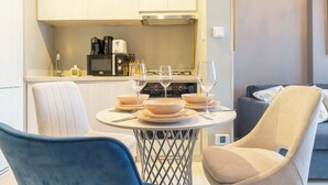 A modern living room with a dining table set for four, a sofa, and a kitchen in the background. - Cosy Unit in Business Bay Sleeps 2 With Canal View (Dubai)
