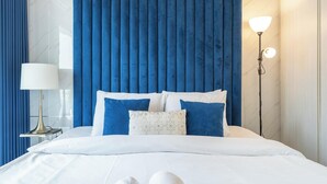 A neatly made bed with white bedding and blue pillows, a bedside lamp, and a wall with vertical blue panels. - Cosy Unit in Business Bay Sleeps 2 With Canal View (Dubai)
