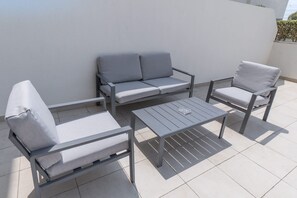 A patio with a grey sofa, two armchairs, and a small table. - Meydan Apartment Sleeps 2 With Huge Balcony (Dubai)