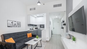 A modern living room with a black sofa, a white coffee table, and a TV on a white wall. - Cozy JVC Studio for 2 With Balcony (Dubai)