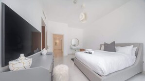A modern bedroom with a large bed, a vanity with a mirror, a fluffy white stool, and a television. - Downtown Dubai Stunning Apartment for 4 People (Dubai)