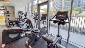 A gym with cardio machines and weight equipment, large windows, and a view of a cityscape. - Downtown Dubai Stunning Apartment for 4 People (Dubai)