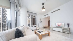 A modern living room with a sofa, coffee table, and a TV displaying "BOOK ME". - Downtown Dubai Stunning Apartment for 4 People (Dubai)