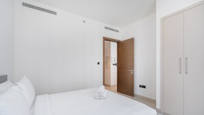A modern hotel room with a neatly made bed, a wardrobe, and a door leading to another room. - Chic 2 bed Apartment in Sobha Creek Vistas (Dubai)