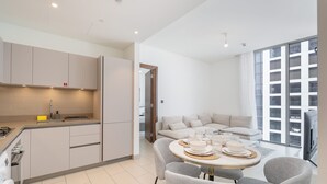 A modern kitchen with a dining area, a sofa, and a large window. - Chic 2 bed Apartment in Sobha Creek Vistas (Dubai)