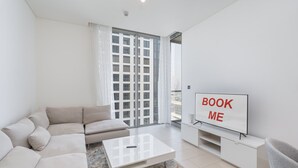 A modern living room with a sofa, coffee table, and a TV displaying "BOOK ME". - Chic 2 bed Apartment in Sobha Creek Vistas (Dubai)