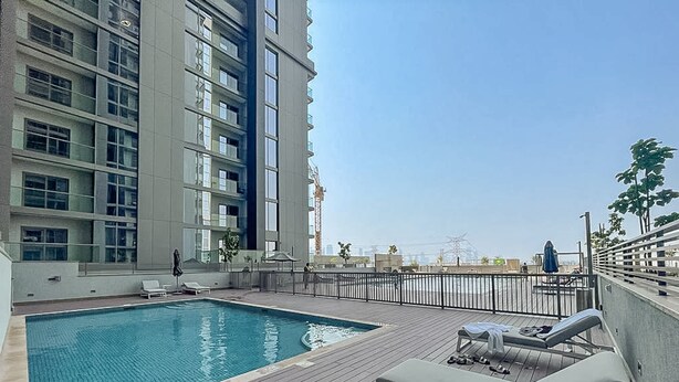 A rooftop pool area with a swimming pool, lounge chairs, and a view of a high-rise building. - Chic 2 bed Apartment in Sobha Creek Vistas (Dubai)