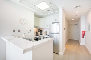 A modern kitchen with white cabinetry, a stainless steel refrigerator, and a built-in island with a sink. - Dubai Marina Spacious 1 bed Unit for 2 People (Dubai)
