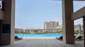 A pool area with wooden decking, lounge chairs, and a view of high-rise buildings in the background. - Chic Studio in Palm Jumeirah Sleeps 2 With Balcony (Dubai)