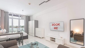 A modern living room with a glass coffee table, grey sofas, a TV mounted on the wall, and a view of the city through large windows. - Chic Studio in Palm Jumeirah Sleeps 2 With Balcony (Dubai)