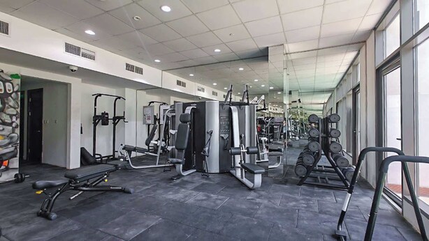 A modern gym with various exercise machines, a bench, and dumbbells. - JVC Apartment That Sleeps 4 With a Great Pool (Dubai)
