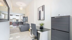 A modern kitchen with white cabinets, a grey sofa, and a desk with a plant. - JVC Apartment That Sleeps 4 With a Great Pool (Dubai)