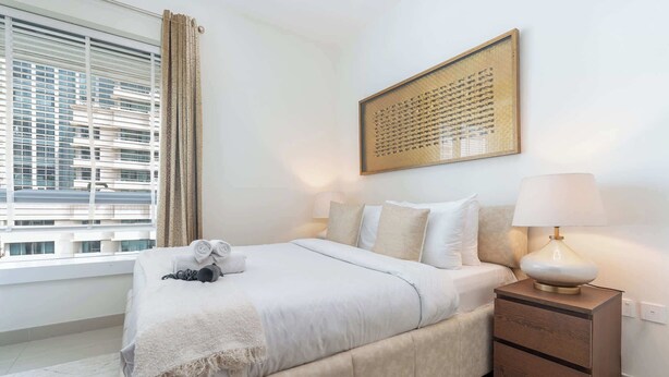 A hotel room with a bed, a nightstand, a lamp, a window with curtains, and a cityscape view. - Downtown Dubai Sleeps 4 Close to Burj Khalifa (Dubai)