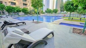 A poolside area with lounge chairs, a swimming pool, and tall buildings in the background. - Downtown Dubai Sleeps 4 Close to Burj Khalifa (Dubai)