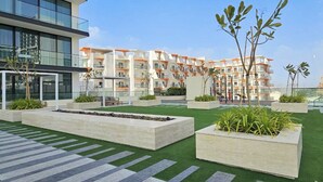 Un immeuble d’appartements moderne doté de nombreux balcons, d’une pelouse artificielle verdoyante et de jardinières rectangulaires contenant des plantes.