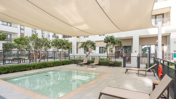 A swimming pool with lounge chairs, surrounded by a covered patio area with plants and a lifebuoy. - Dubai Creek Harbour Sleeps 4 With Swimming Pool (Dubai)