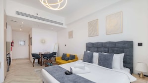 A modern hotel room with a large bed, a sofa, a dining area, and a hallway. - JVC Studio for 3 People With Swimming Pool (Dubai)