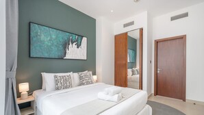 Ein ordentlich eingerichtetes Schlafzimmer mit einem großen Bett, einem Nachttisch mit Lampe, einem Wandbild, einem Holzschrank und einer Tür.