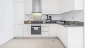 Eine moderne Küche mit weißen Schränken, einer Edelstahl-Dunstabzugshaube, einem eingebauten Backofen, einer Kaffeemaschine und einem Spülbecken mit Armatur.