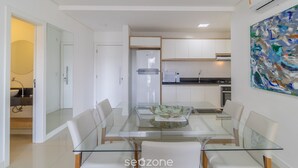 A modern kitchen with white cabinets, a glass dining table, and a contemporary painting on the wall.