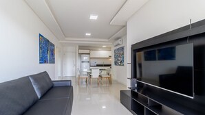A modern living room with a large flat-screen TV, a grey sofa, and artwork on the walls.