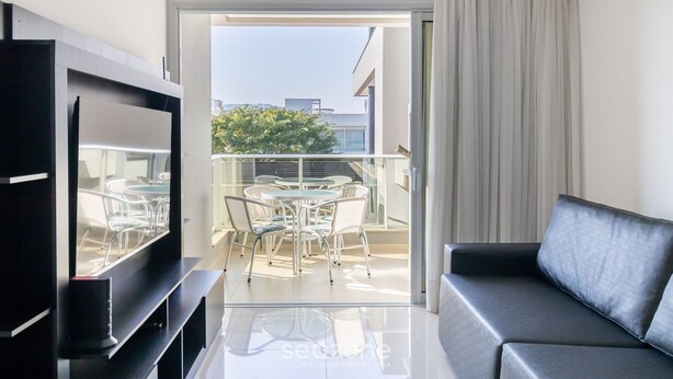 A modern living room with a flat-screen TV, a sofa, and a dining area with a table and chairs.