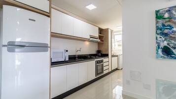 A modern kitchen with white cabinets, a built-in oven, and a stainless steel refrigerator.